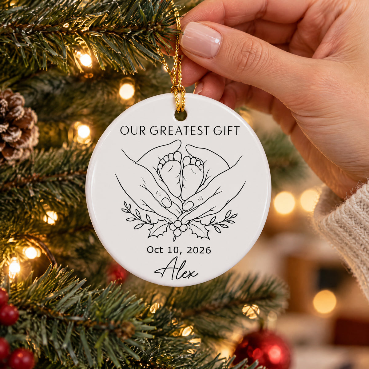 Personalized minimalist line art ornament held by a hand beside a lit Christmas tree and pinecone
