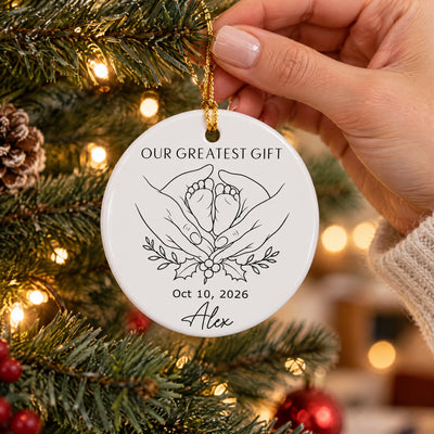 Personalized minimalist line art ornament held by a hand beside a lit Christmas tree and pinecone