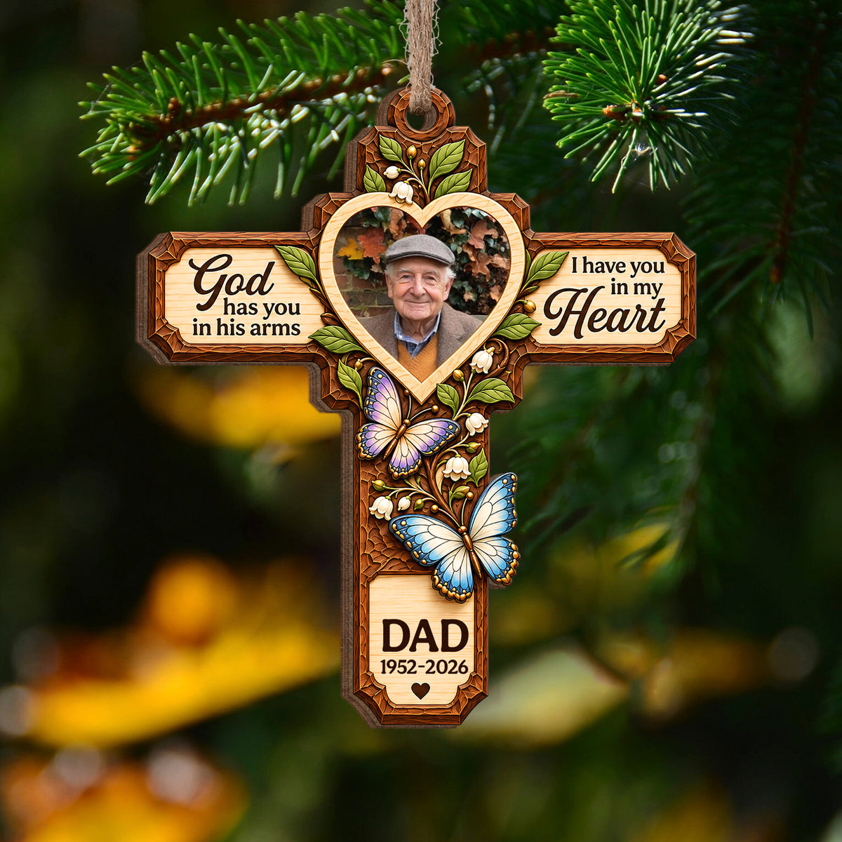 Personalized Memorial Wooden Ornament hanging from a pine branch with blurred yellow leaves behind