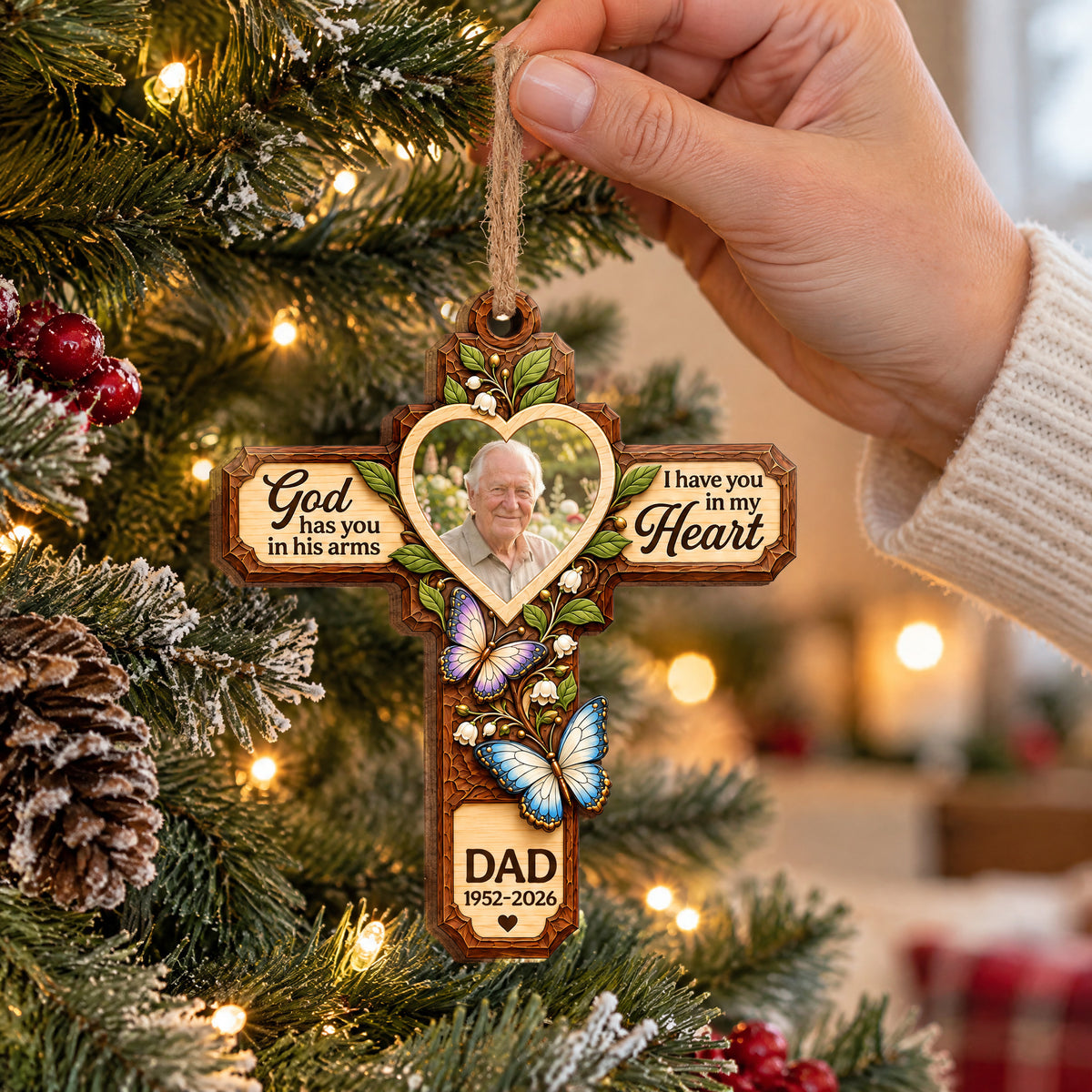 Personalized Memorial Wooden Ornament held by a hand in a cream sweater near a tree with lights and pinecones