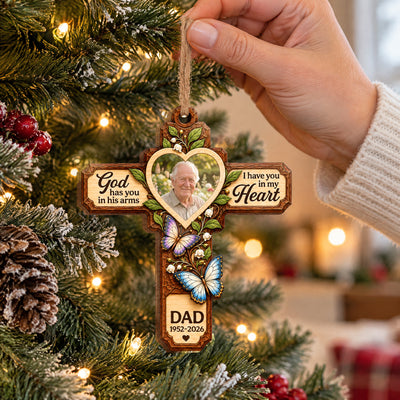 Personalized Memorial Wooden Ornament held by a hand in a cream sweater near a tree with lights and pinecones
