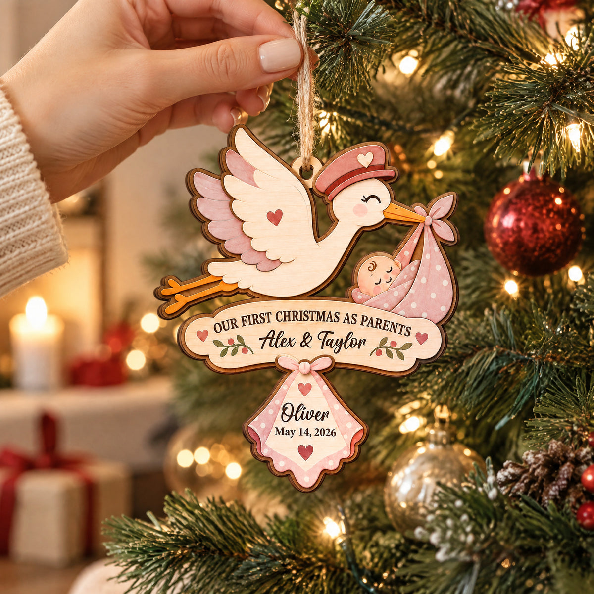 Our First Christmas As Parents Personalized Wooden Ornament held by a hand in front of a lit tree and red bauble
