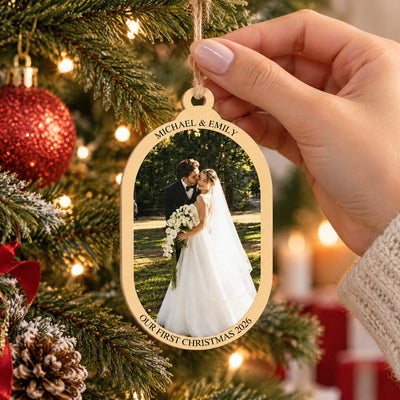 Personalized wooden photo ornament held by a hand by its twine loop in front of a lit Christmas tree