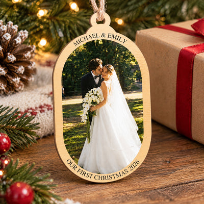 Personalized wooden photo ornament standing on a wood table next to a wrapped gift with red ribbon and pine branches