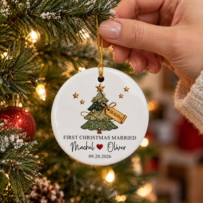 Personalized ceramic ornament First Christmas Married held by a hand beside a lit tree with a red bauble