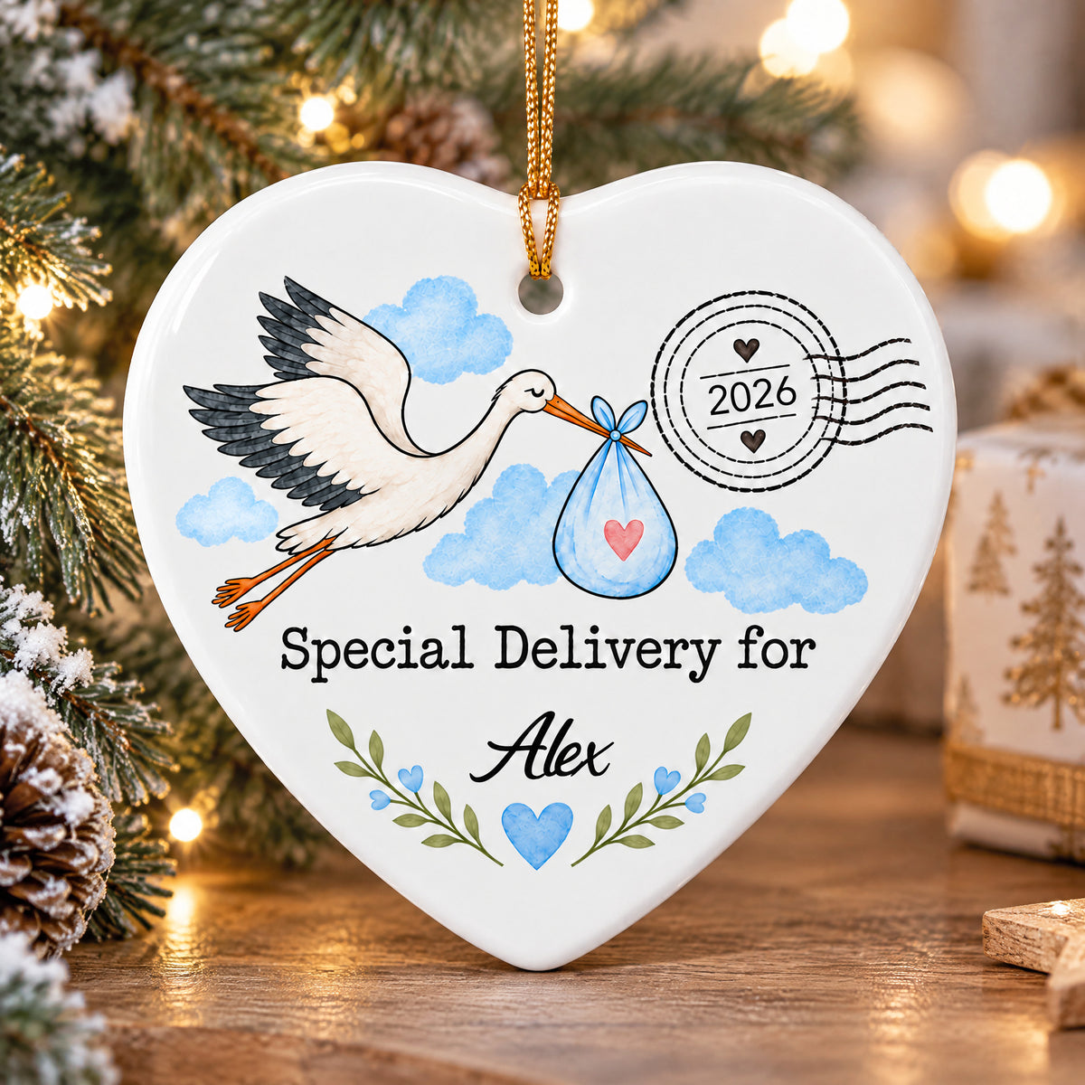 Personalized Stork Special Delivery Ceramic Ornament in blue hanging on a wooden surface beside pinecones and a gift