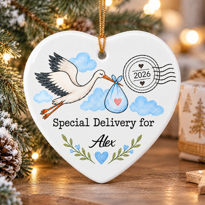 Personalized Stork Special Delivery Ceramic Ornament in blue hanging on a wooden surface beside pinecones and a gift