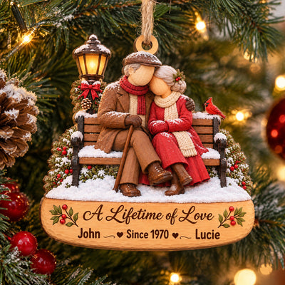 Personalized Wooden Couple Christmas Ornament hanging on a pine branch, couple on a snowy bench with names John and Lucie