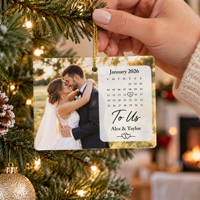 Rectangular ceramic ornament photo calendar held by a hand in a knit sleeve near a tree and fireplace