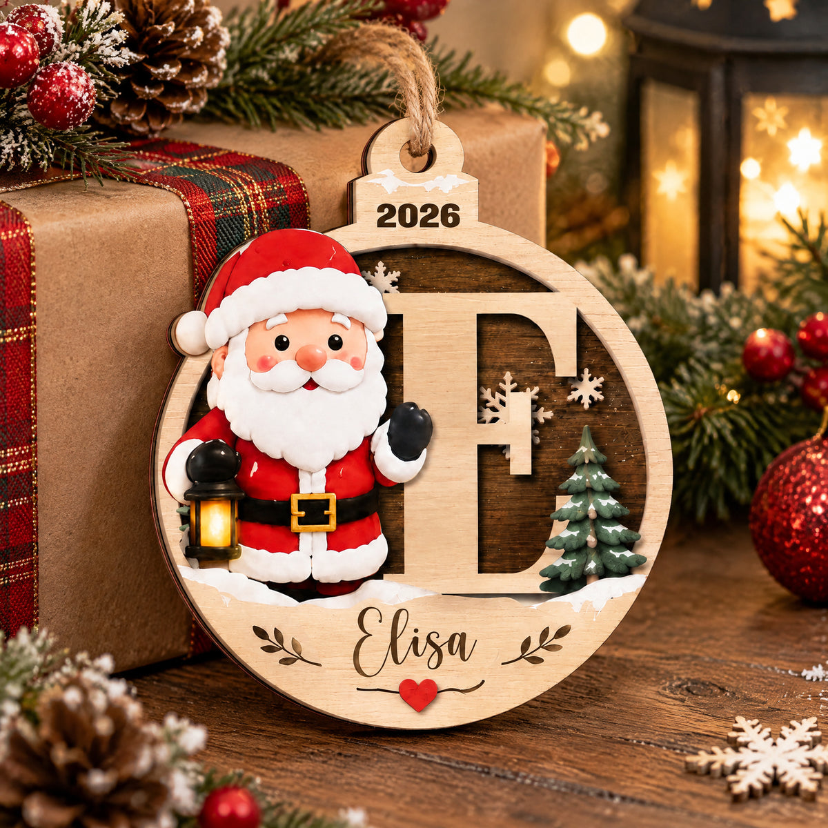 Personalized Santa Initial Wooden Ornament leaning on a wrapped gift with plaid ribbon, lantern and snowflake nearby