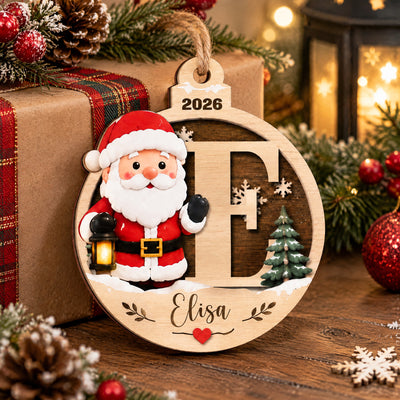 Personalized Santa Initial Wooden Ornament leaning on a wrapped gift with plaid ribbon, lantern and snowflake nearby