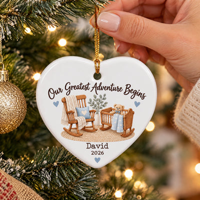 Personalized Ceramic Ornament Our Greatest Adventure Begins held by hand near tree lights and gold bauble