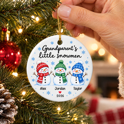 Personalized Grandparent's Little Snowmen Ceramic ornament held up on a pine branch with a fireplace behind