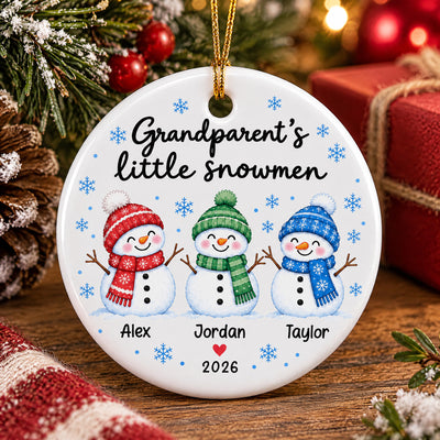 Personalized Grandparent's Little Snowmen Ceramic ornament on a wooden table beside a red gift and pinecone