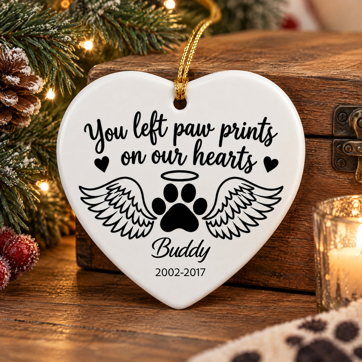 Personalized ceramic angel wings pet memorial ornament resting on a wooden box beside a candle and pinecones