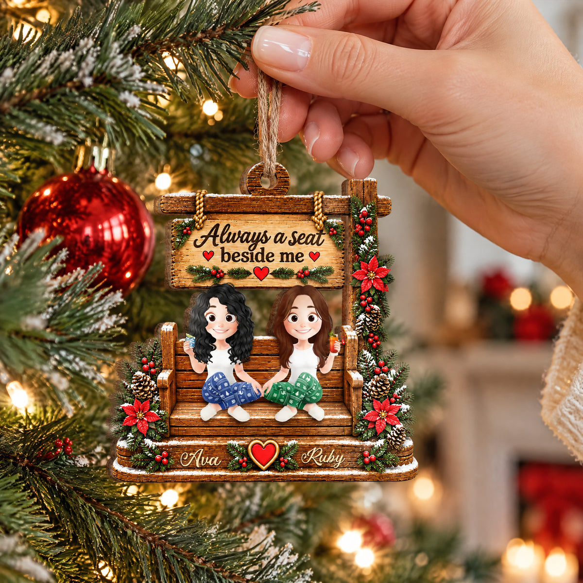 Personalized wooden ornament custom name held by hand on twine near a red bauble and a softly lit fireplace