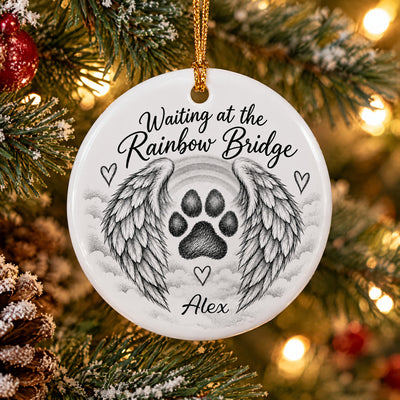 Personalized pet memorial ceramic ornament with name Alex hanging on a frosted pine branch with warm lights