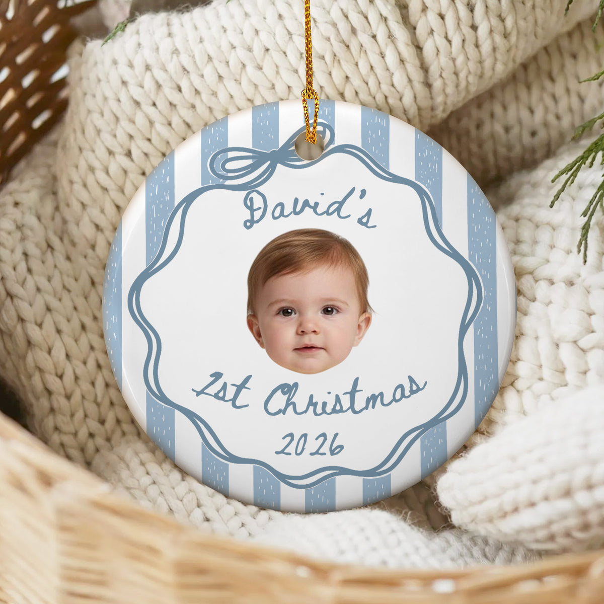 Personalized custom baby face Christmas ornament with blue stripes, resting on a cream knit blanket in a basket