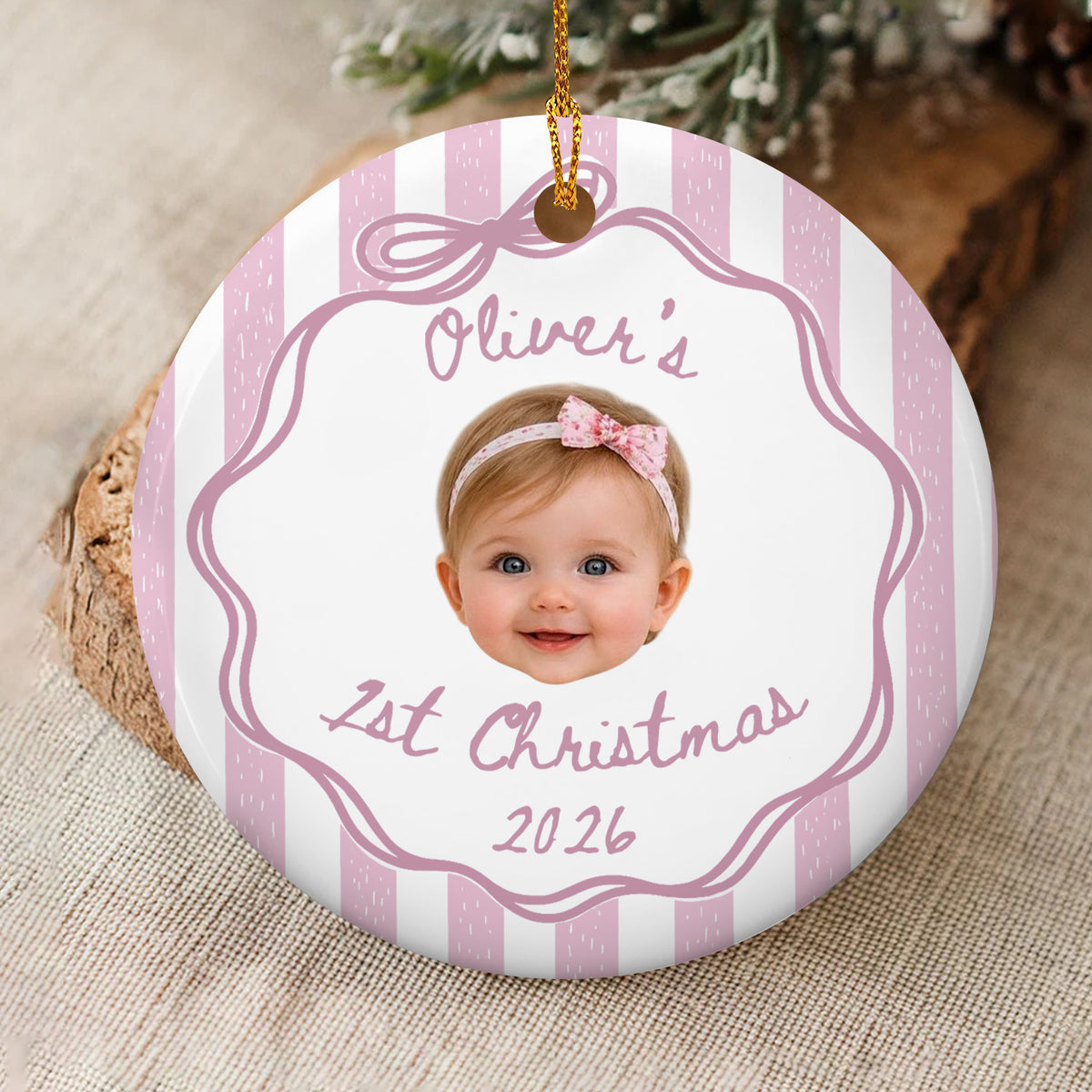 Personalized custom baby face Christmas ornament with pink stripes and a bow headband, lying on a wood slice