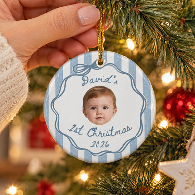 Personalized custom baby face Christmas ornament in blue, held by a hand beside tree lights and a star