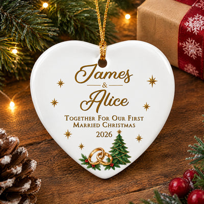 Personalized ceramic ornament first married Christmas heart on a wooden table beside pine and a wrapped gift