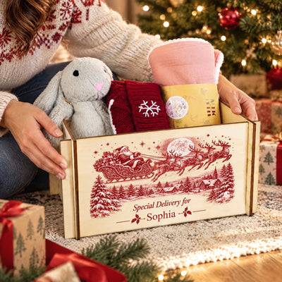 Personalized Christmas Eve Box held by a person in a snowflake sweater, with plush bunny and blanket inside by the tree