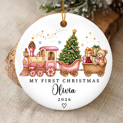 Personalized Custom First Christmas Ceramic Ornament with pink toy train and Olivia name, on burlap beside a wood slice