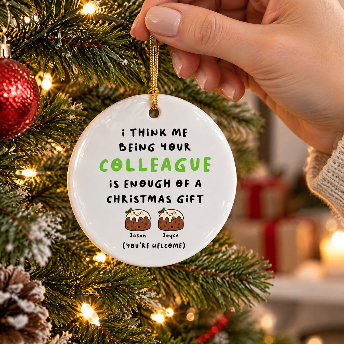 Personalized Colleague Christmas Gift Ceramic Ornament held by its cord beside a tree, with wrapped gifts blurred behind