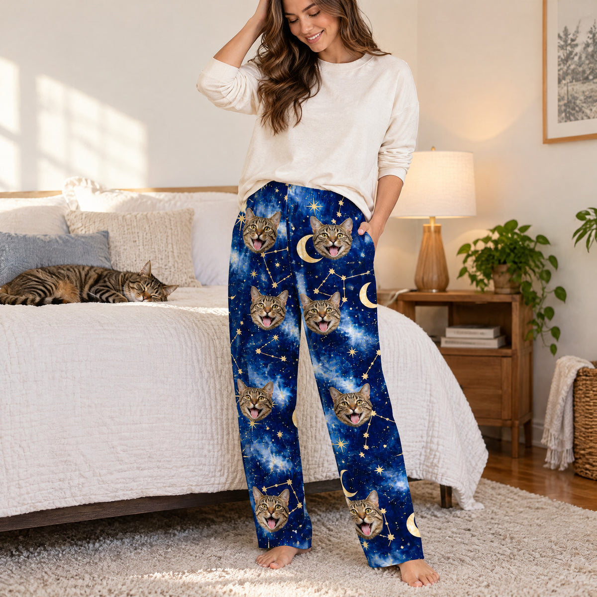 Custom pet photo personalized pajama pants on a smiling woman in a bedroom, with a tabby cat resting on the bed