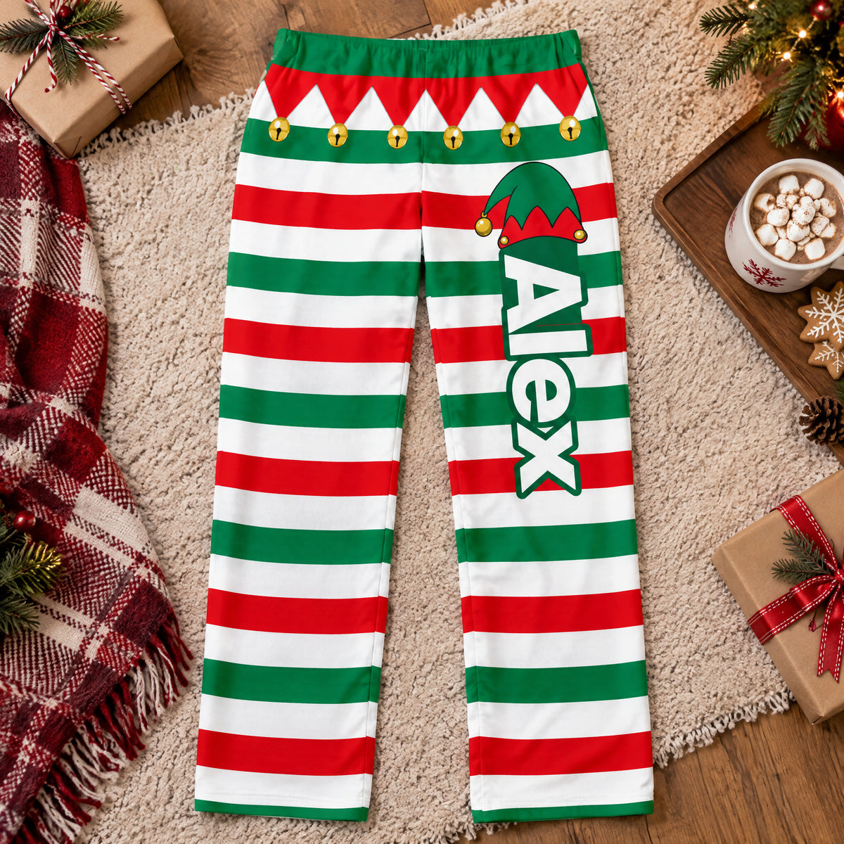 Personalized Elf Pajama Pants laid flat on a rug with a blanket, cocoa and gifts around