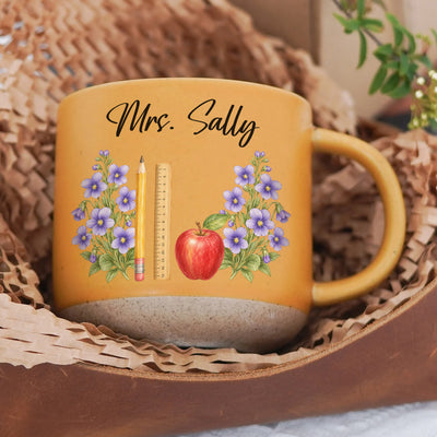 Personalized pottery mug custom teacher name orange mug with purple flowers resting in paper filling inside a basket