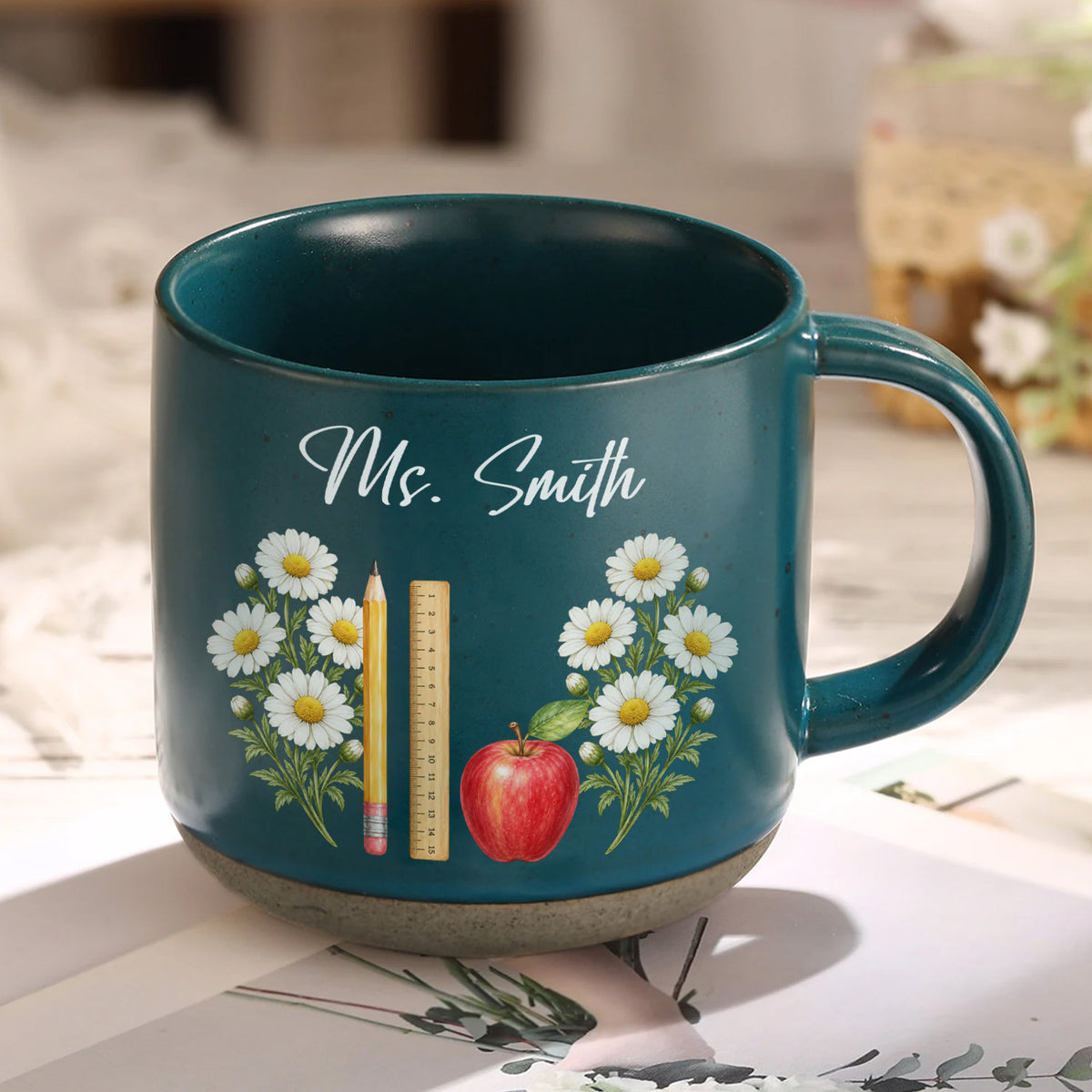 Personalized pottery mug custom teacher name dark teal mug with white daisies, pencil, ruler and apple on a tabletop