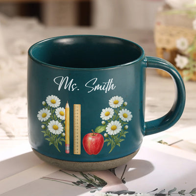 Personalized pottery mug custom teacher name dark teal mug with white daisies, pencil, ruler and apple on a tabletop