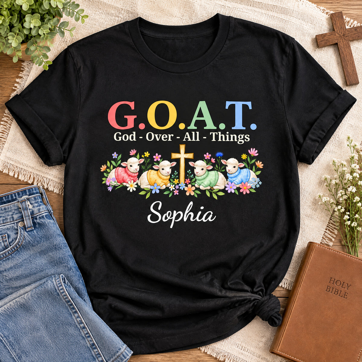 Personalized G.O.A.T. God Over All Things Shirt laid flat with jeans, wooden cross, Bible and dried flowers