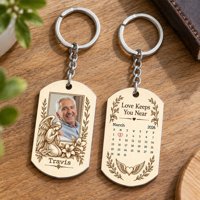 Personalized Stainless Steel Memorial Keychain on a wooden table beside green leaves, front and back both in view