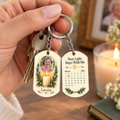 Personalized stainless steel memorial keychain hanging beside house keys, with a lit candle and framed photo behind