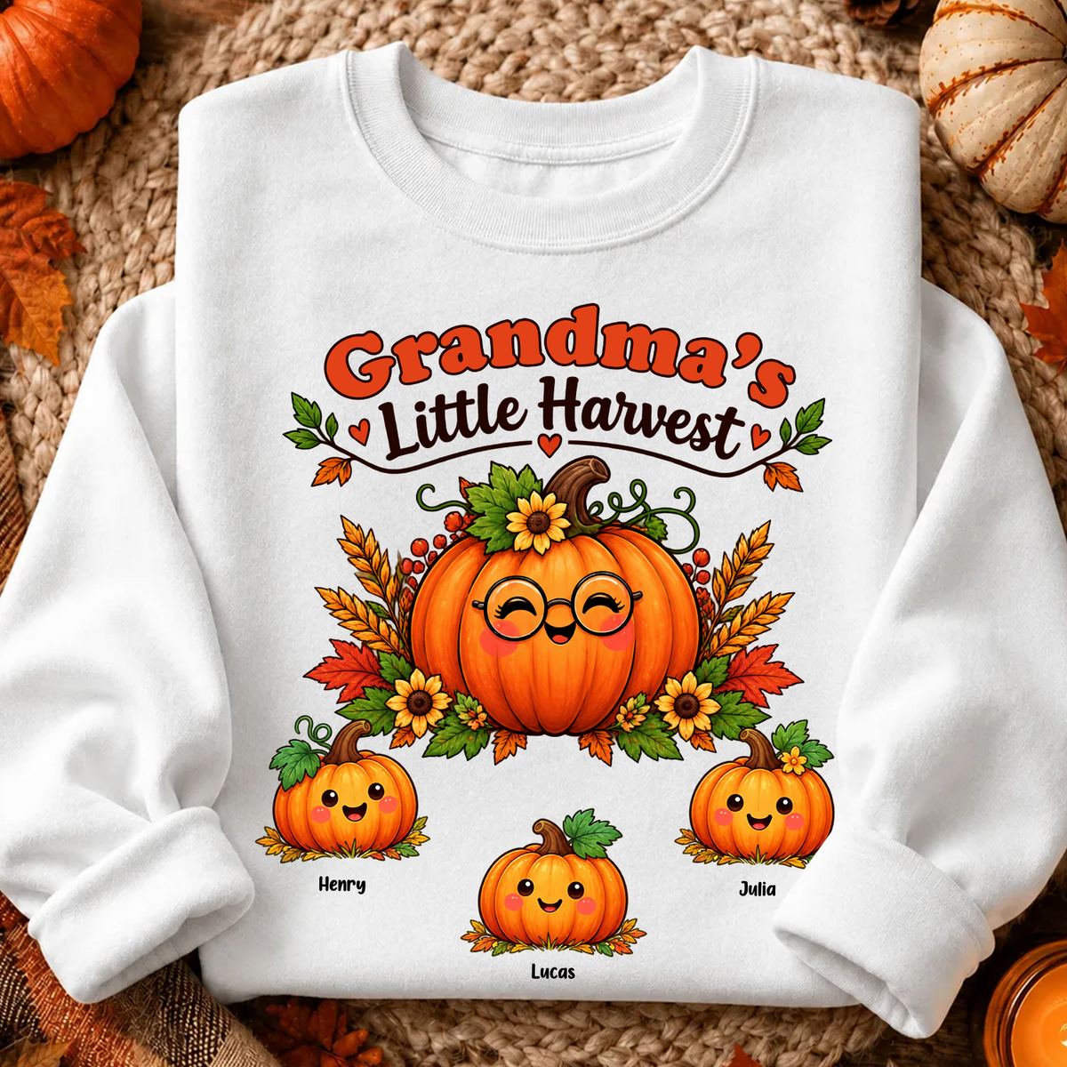 Grandma's Little Harvest Personalized Sweatshirt laid flat on a woven mat with leaves and three pumpkin names