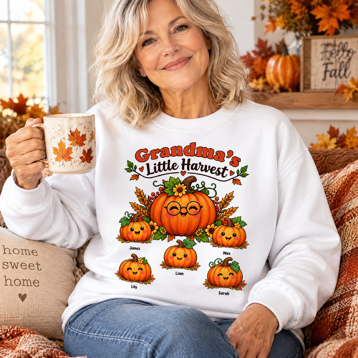 Grandma's Little Harvest Personalized Sweatshirt worn by a smiling woman holding a mug on a cozy fall sofa