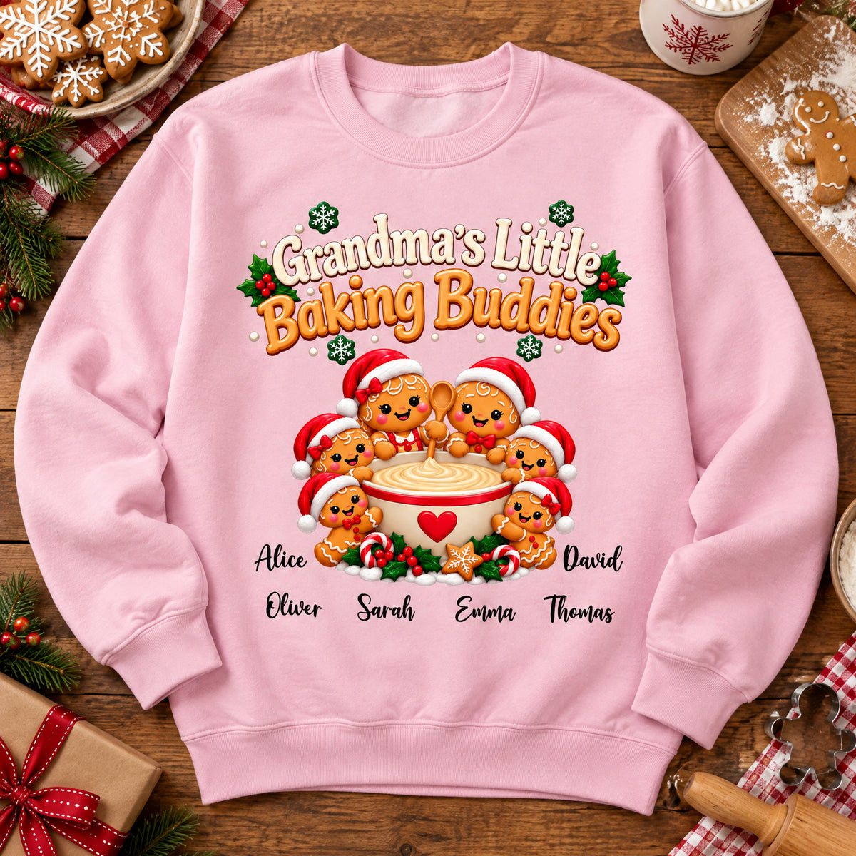 Grandma's Little Baking Buddies Personalized Sweatshirt in pink laid flat on a wooden table with cookies and a gift