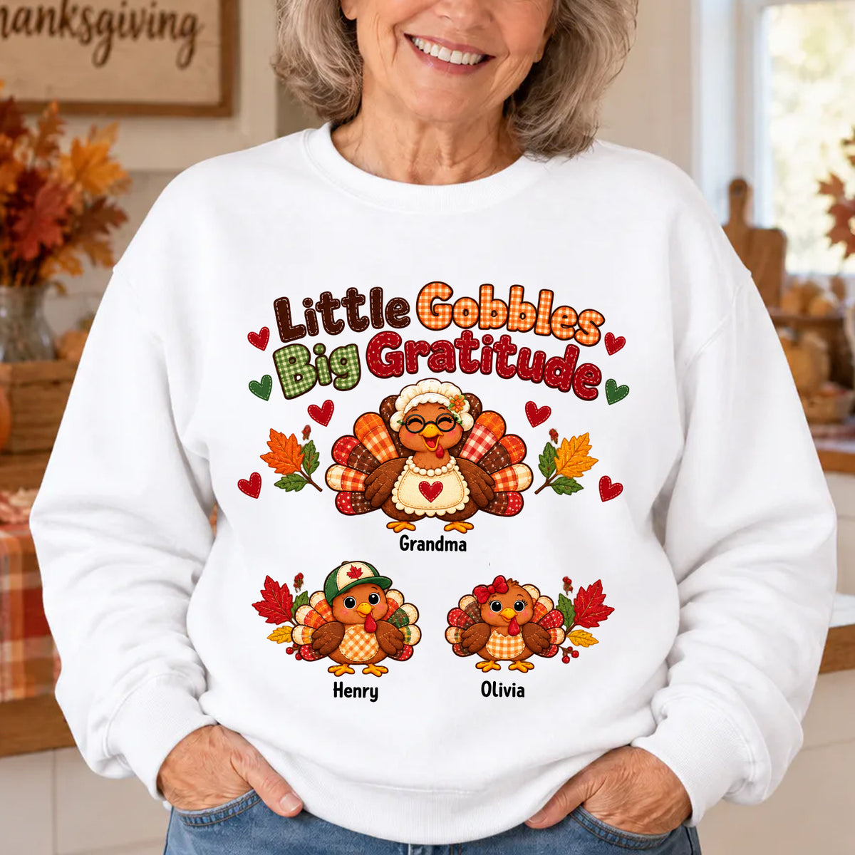 Personalized Little Gobbles Big Gratitude Sweatshirt in white worn in a kitchen, three turkeys named Grandma, Henry, Olivia