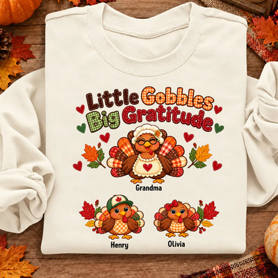 Personalized Little Gobbles Big Gratitude Sweatshirt in cream, folded flat with autumn leaves and plaid cloth around it