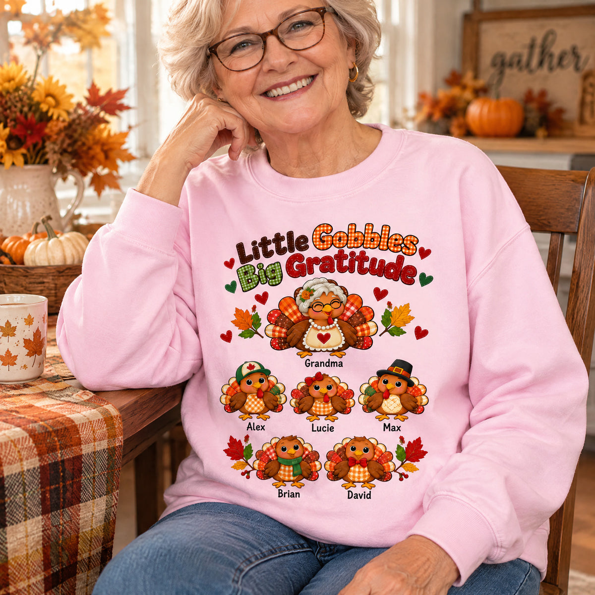 Personalized Little Gobbles Big Gratitude Sweatshirt in pink on a seated woman at a table with pumpkins and flowers