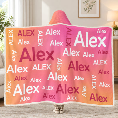Personalized Wearable Hooded Blanket in pink and orange with Alex name pattern, worn from behind in a living room