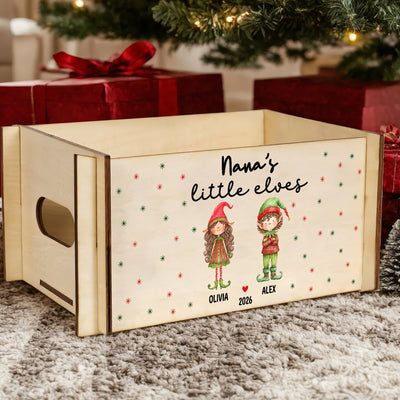 Personalized wooden treasure chest with two elves and names on front, resting on a gray rug by red gift boxes