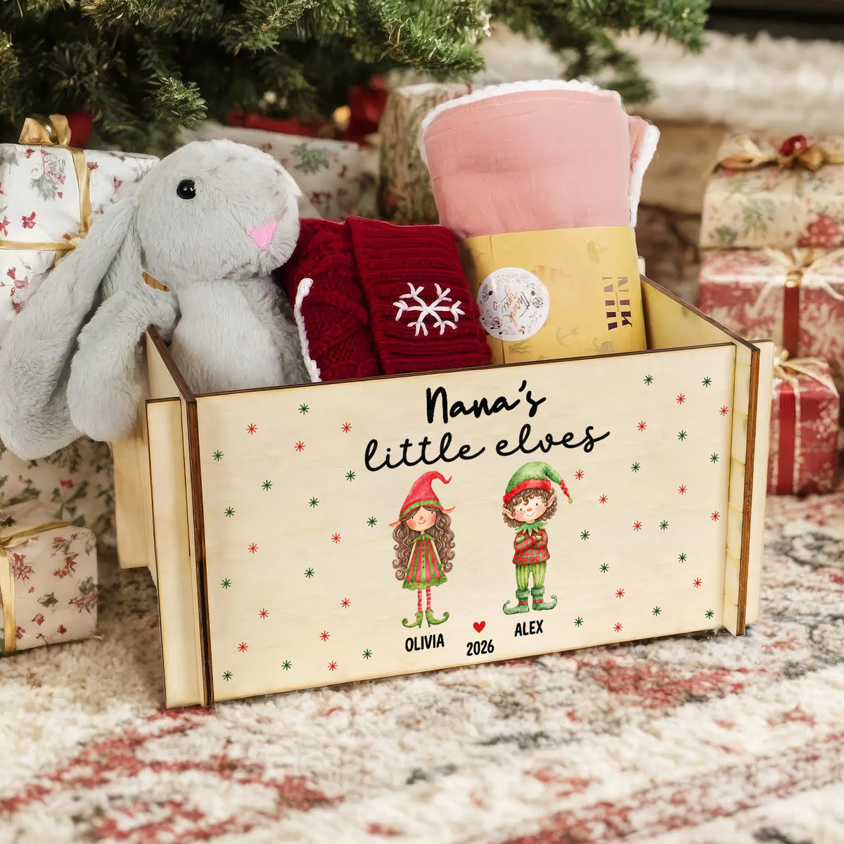 Personalized wooden treasure chest holding a gray plush bunny, red knit items and a folded pink blanket by wrapped gifts
